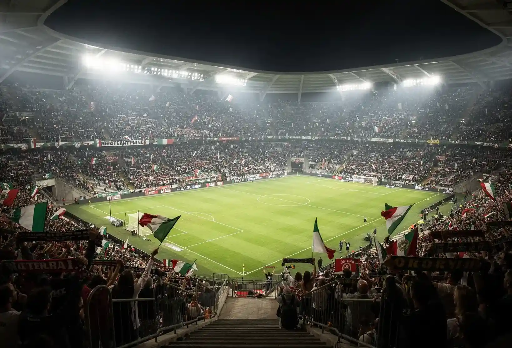 Stadio di calcio italiano illuminato durante partita serale con tifosi sugli spalti